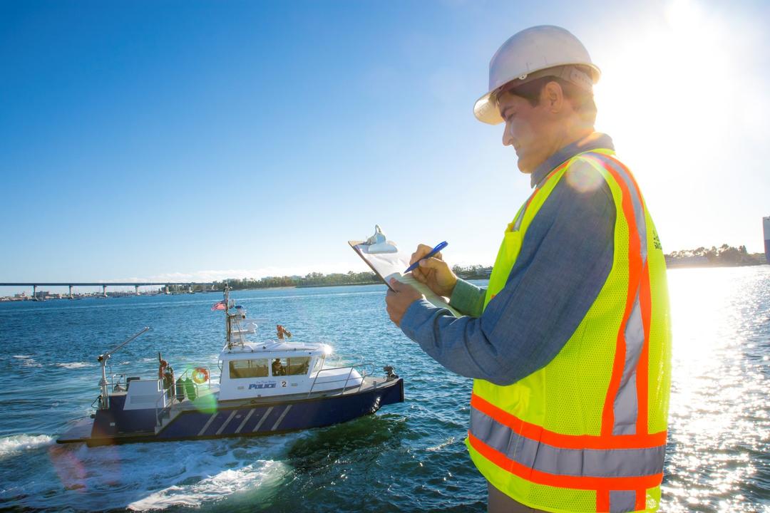 a worker takes notes on a clipboard as the Port of San Diego Harbor Police boat goes by in the San Diego Bay