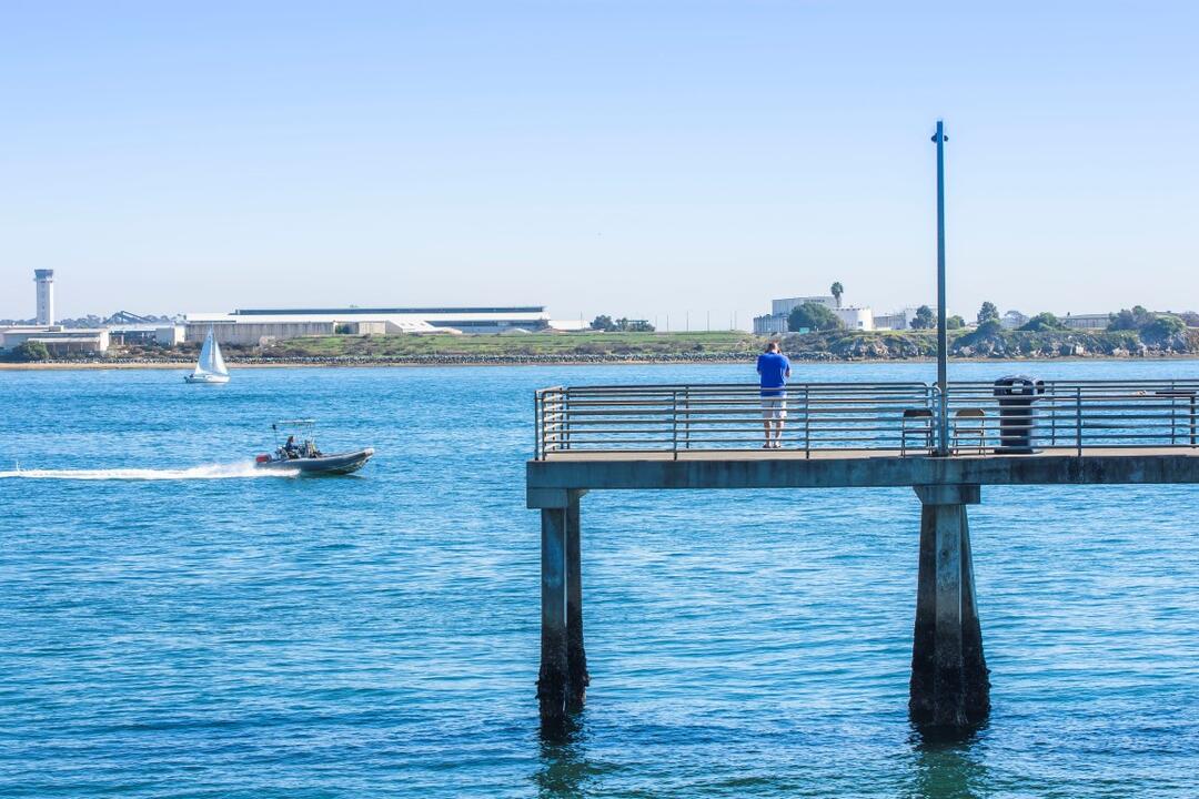 Man taking a photo from the pier of the speedboat on the bright blue water under light blue skies