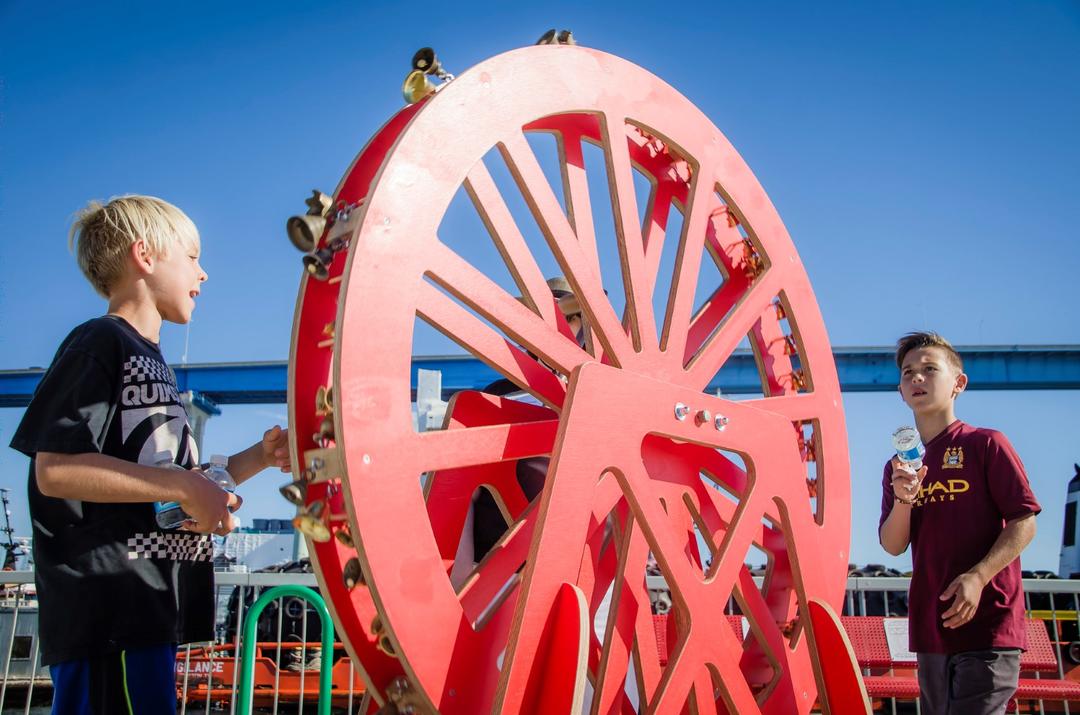 two boys interact with a big red wheel at Time Strata by Margaret Noble