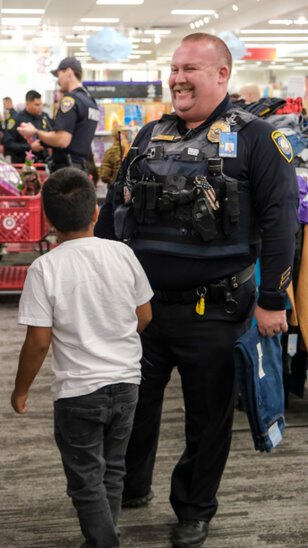 A police officer shopping with a boy with other officers in the background.