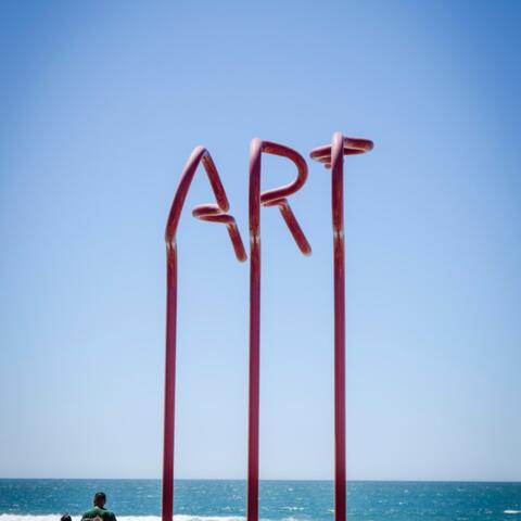 3 red vertical lines reach up and spell out the word "ART" in front of the beach in Imperial beach.