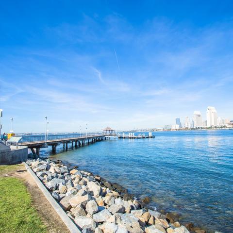 Rocks, water, pier, blue skies, and view of Downtown cityscape at Coronado Landing Park at the Port of San Diego