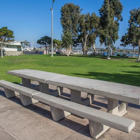 Long picnic tables surrounded by green grass and trees at Pepper Park at the Port of San Diego