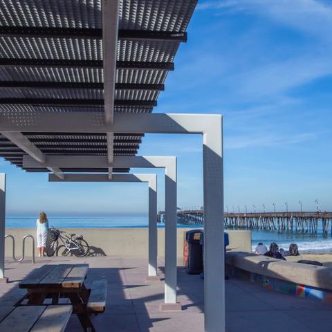Picnic tables under awnings overlooking the beach and pier at Portwood Pier Plaza at the Port of San Diego