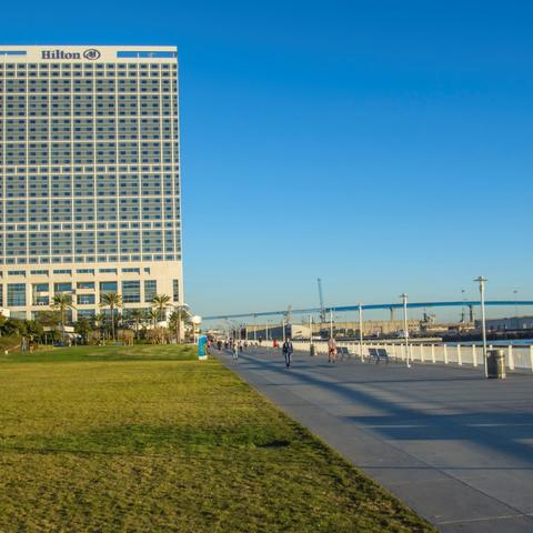 View of Hilton hotel, San Diego-Coronado Bay Bridge, grass, and path at San Diego Bayfront Park at the Port of San Diego
