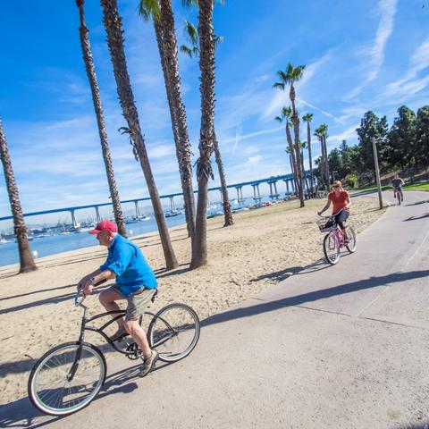 Cyclists biking on path with view of San Diego-Coronado Bay Bridge at Coronado Tidelands Park at the Port of San Diego