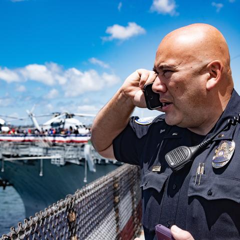 A Port of San Diego Harbor Police Officer is talking on a communication device overlooking the USS Midway