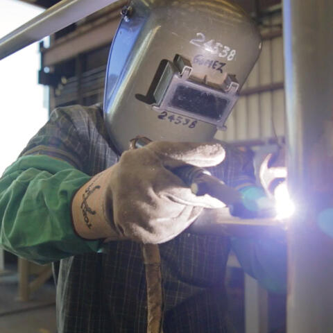 a person welds a metal pole. They are wearing a helmet and other protective clothing